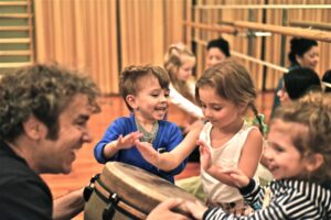 Young children exploring drums, shakers, and movement in a joyful group music session focused on hands-on, screen-free learning.