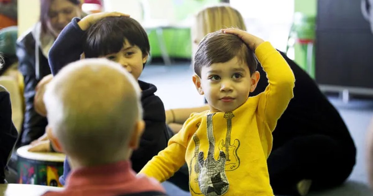 A boy in a yellow shirt holding his head and grinning during music