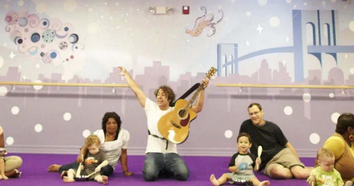 A teacher playing guitar for grown-ups and babies on a purple floor