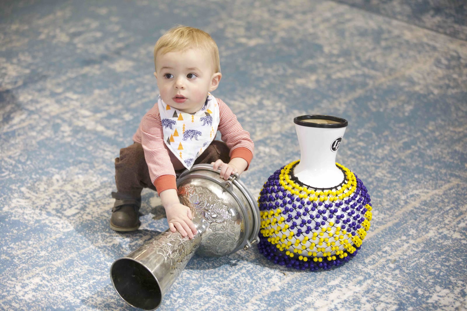A toddler exploring a shekere and drum on the classroom rug