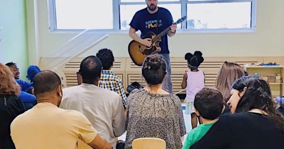 A teacher playing guitar for a classroom of seated children