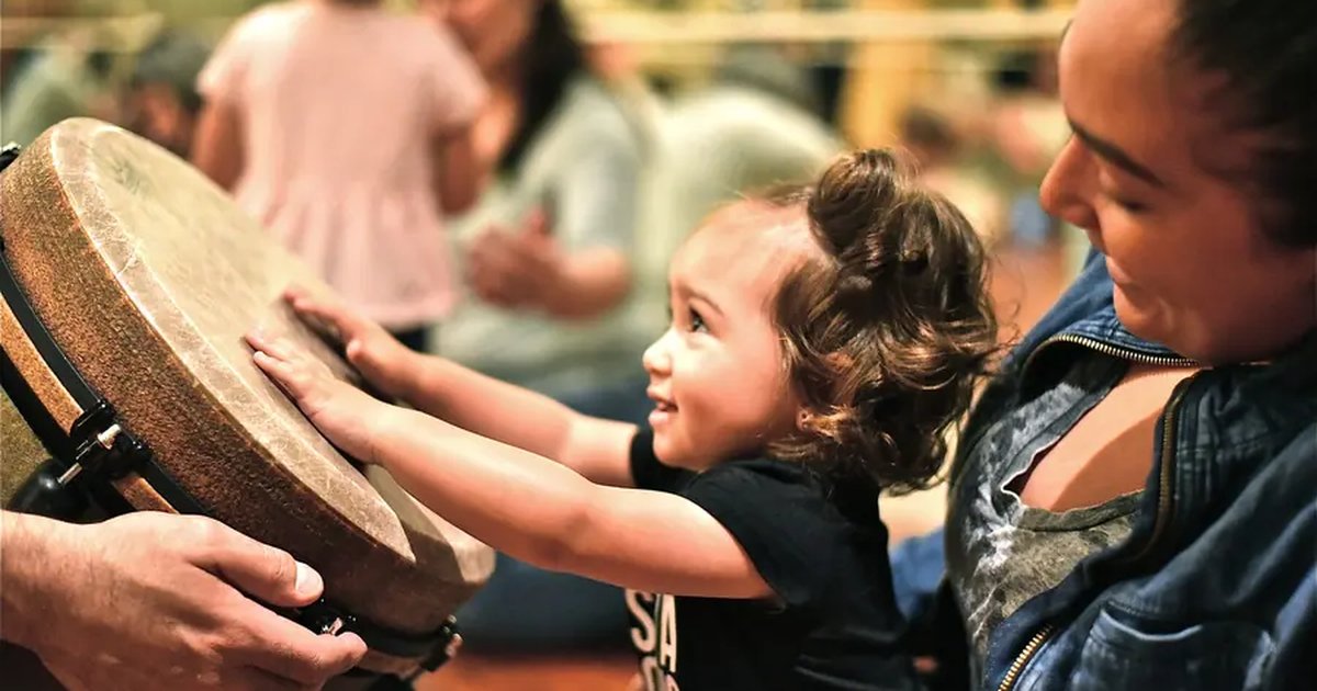 A toddler reaching out to tap a hand drum