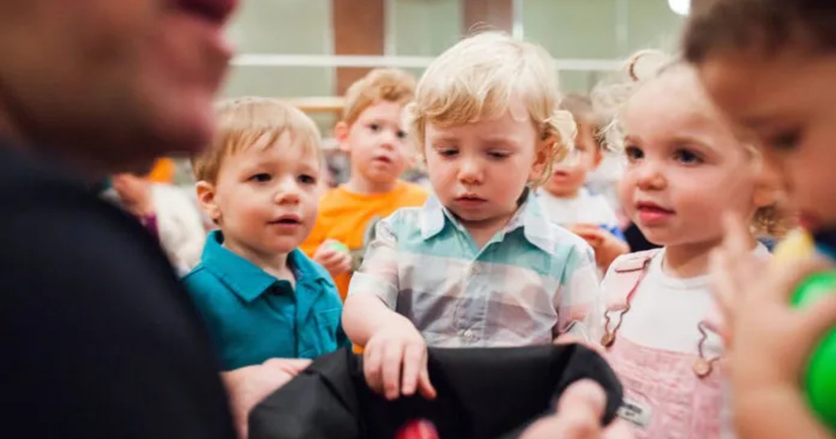 Toddlers dropping shaker balls into a black bag held by the teacher