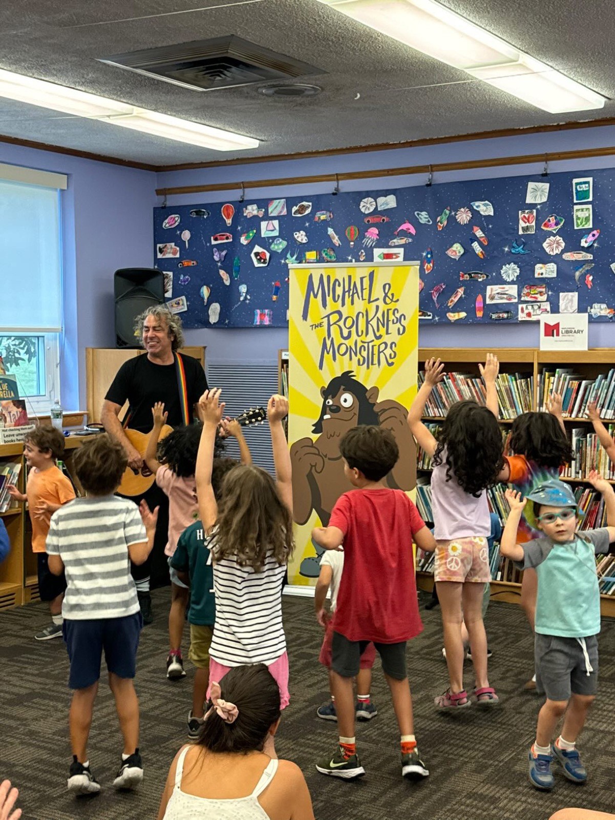 Michael Napolitano playing guitar for dancing kids at a library concert