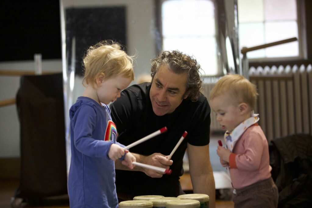 A music educator guiding children through an interactive class where students listen, move, and play instruments with full attention and excitement.